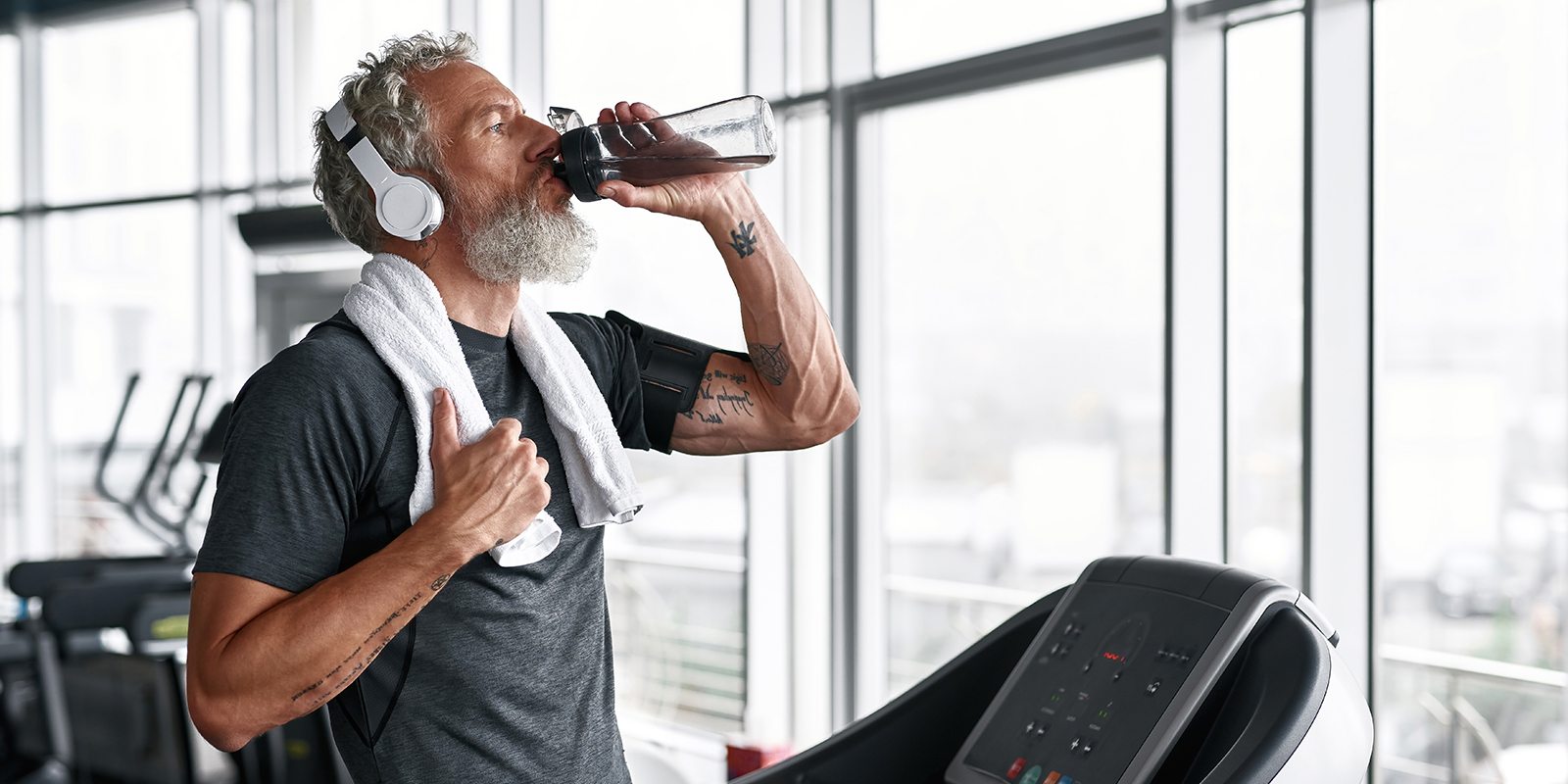 Man on treadmill, drinking water with towel around his neck
